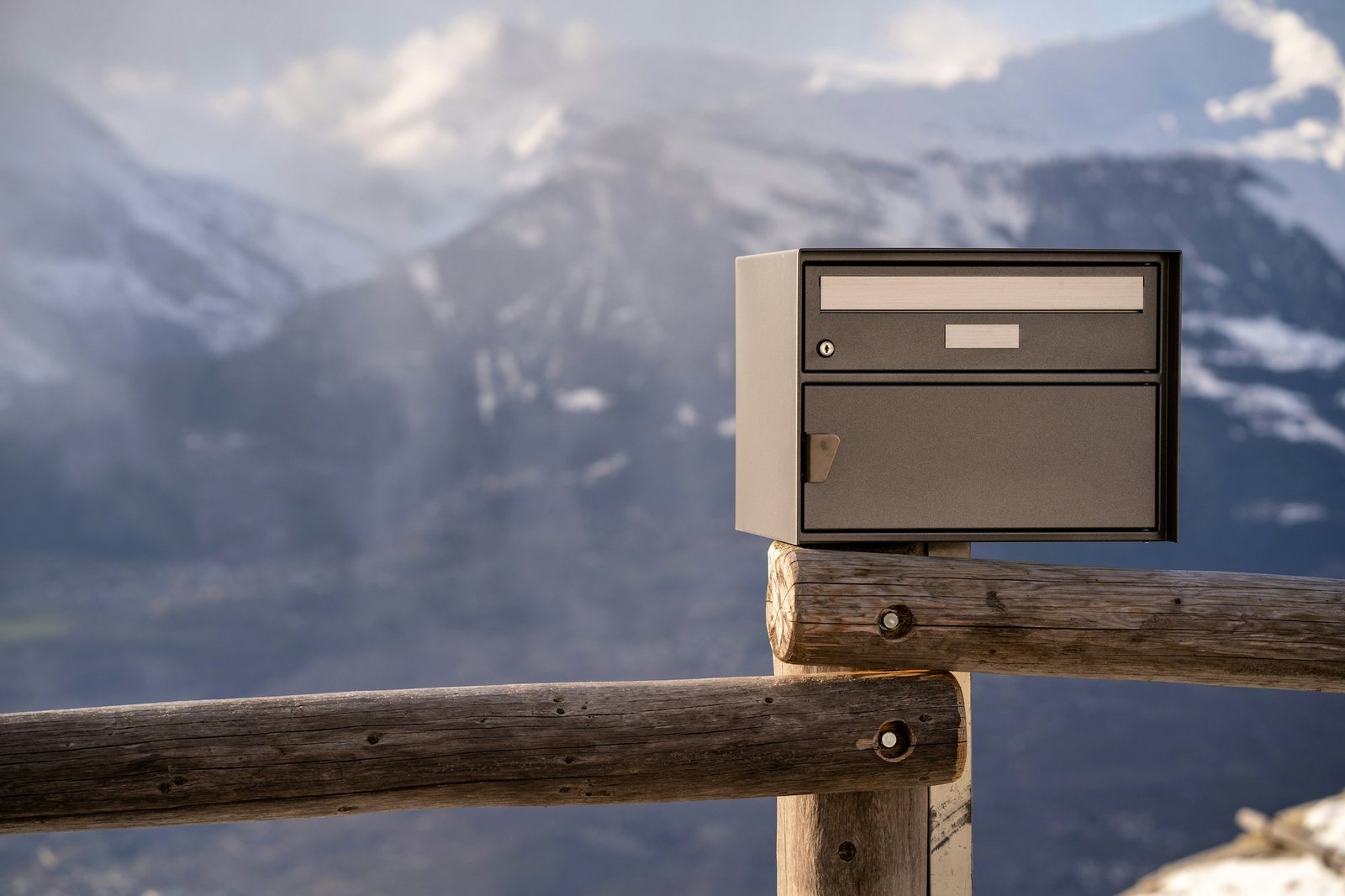 Grey letterbox on a wooden fence with mountains behind