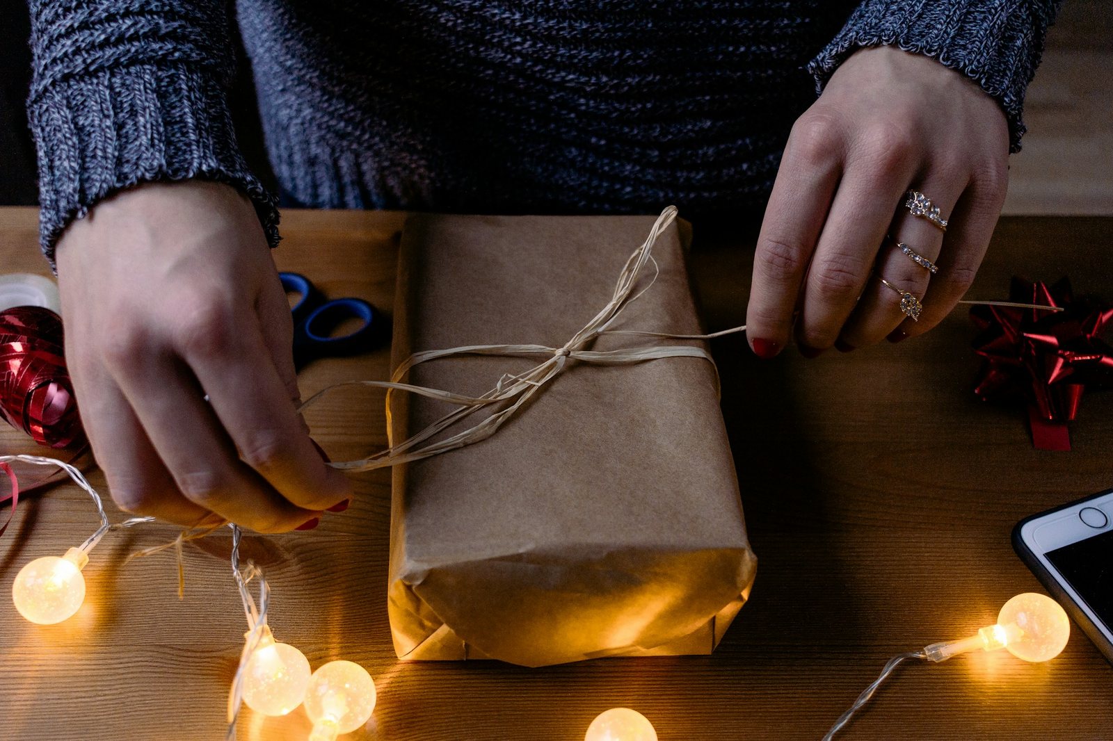 Hands tying twine on a paper-wrapped parcel beside string lights